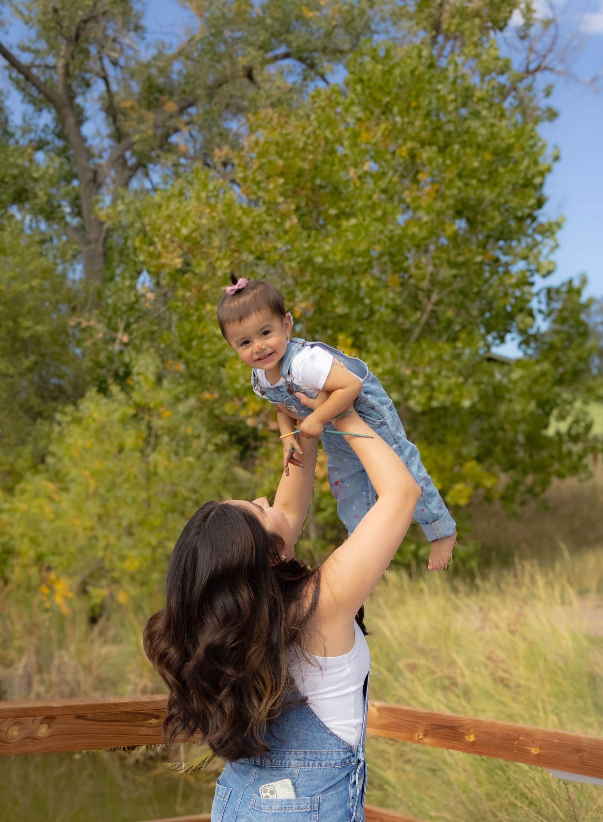 A woman is holding a baby in her arms over a wooden bridge.