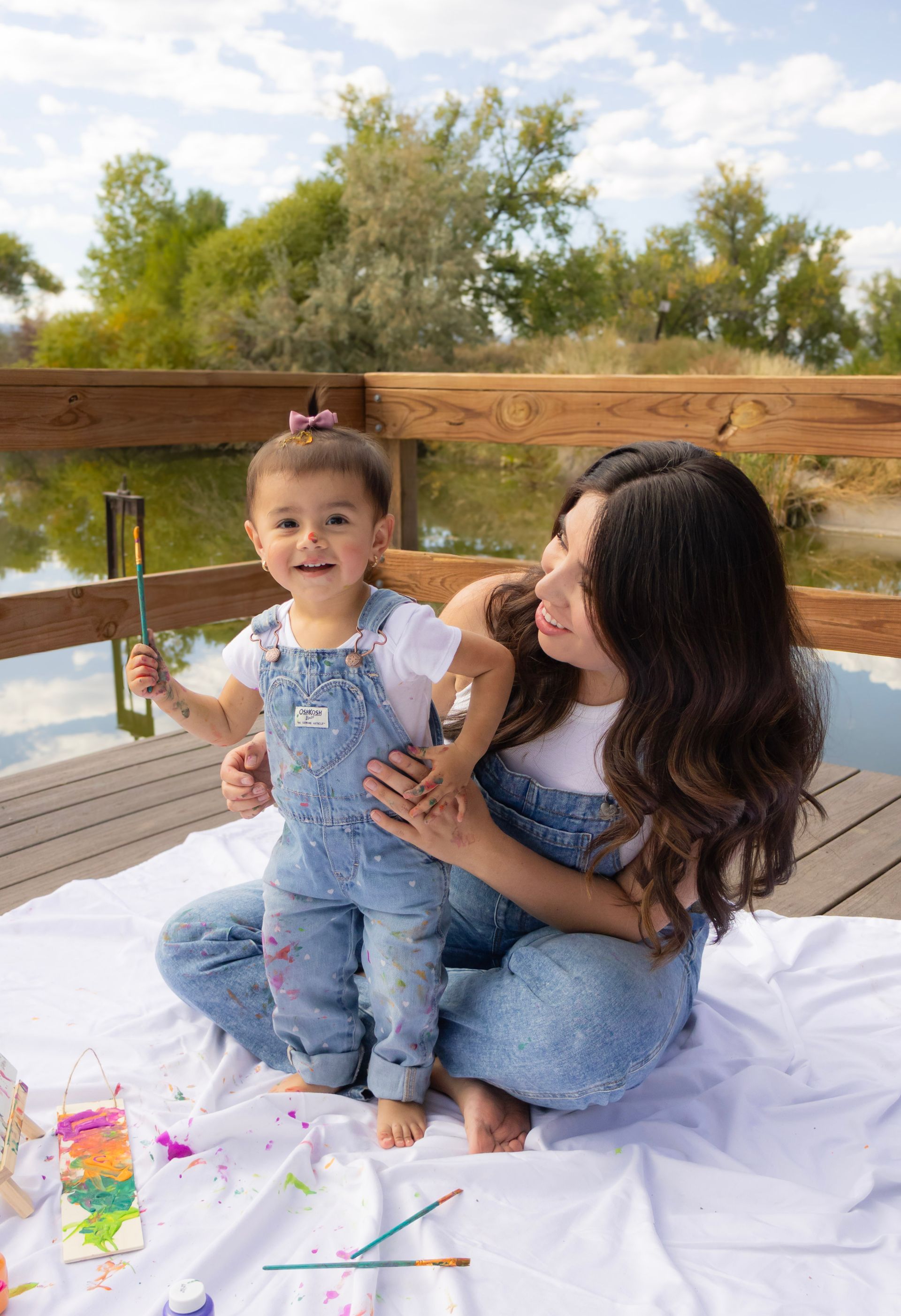 A woman and a little girl are sitting on a blanket on a dock.
