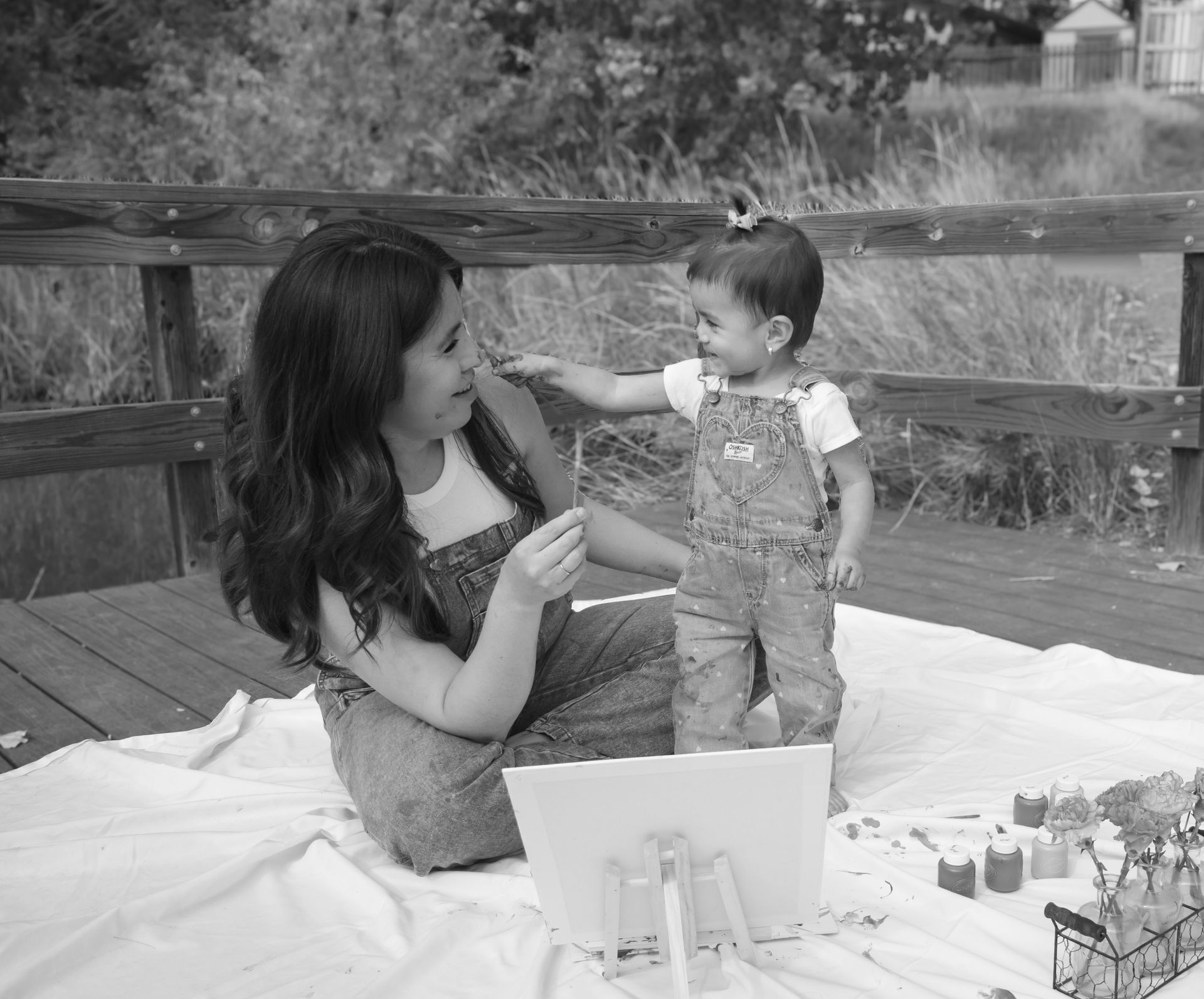 A woman is sitting on a blanket with a baby and a laptop.