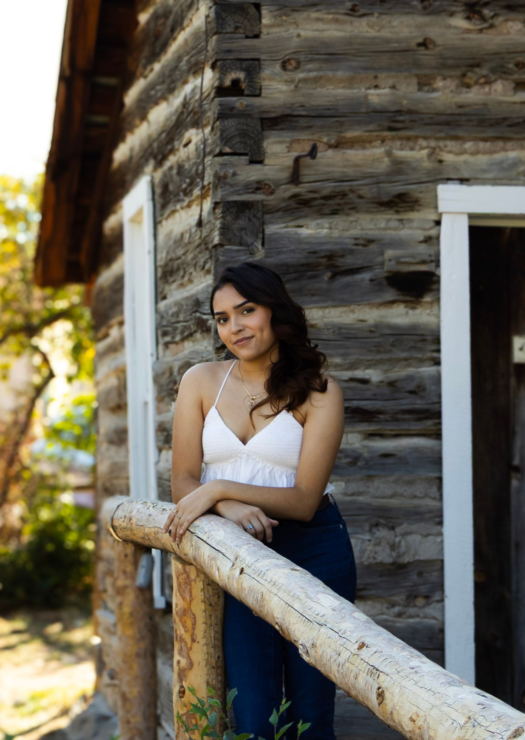 A woman is leaning on a wooden railing in front of a log cabin.