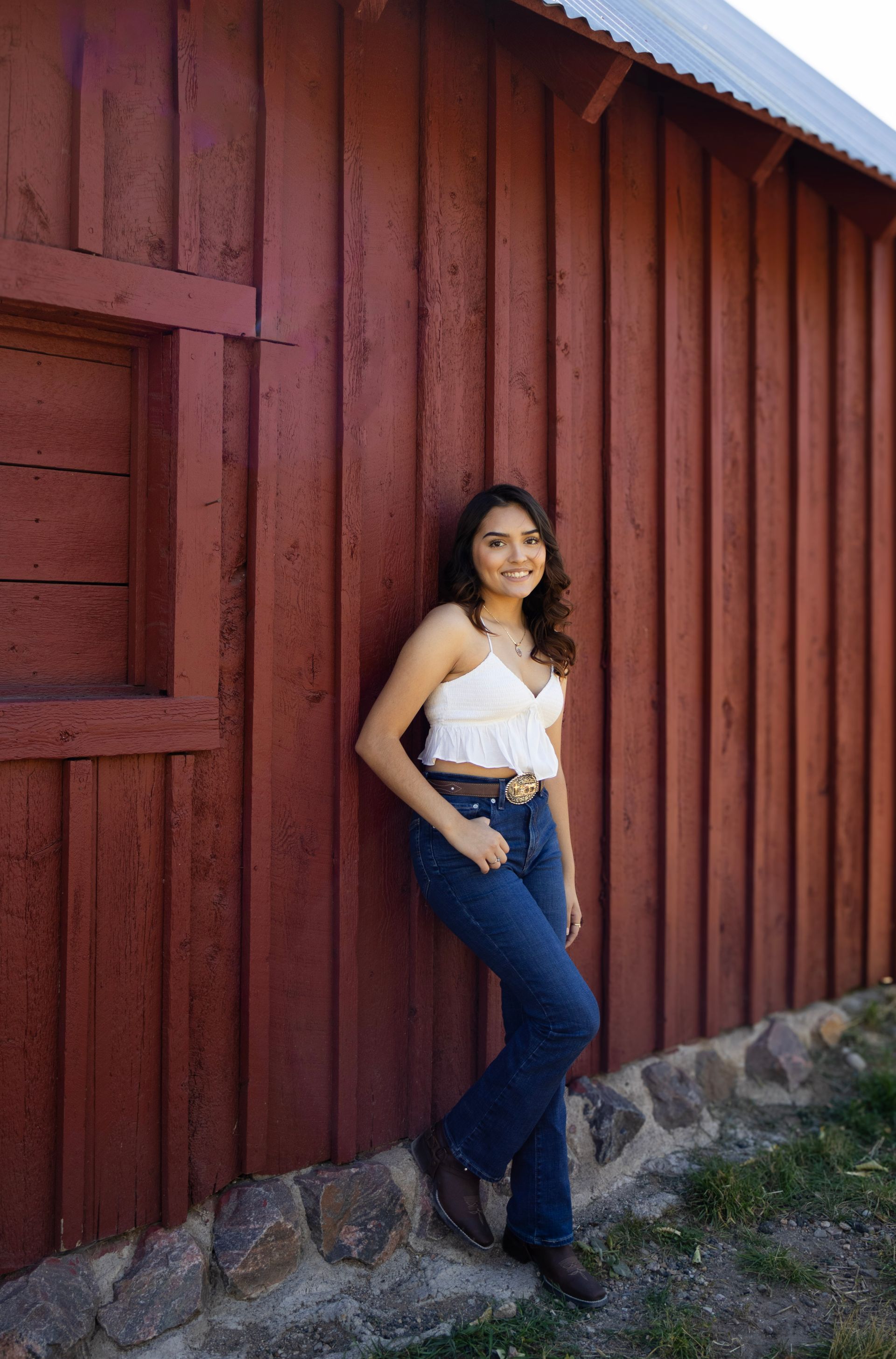 A woman is leaning against a red barn wall.
