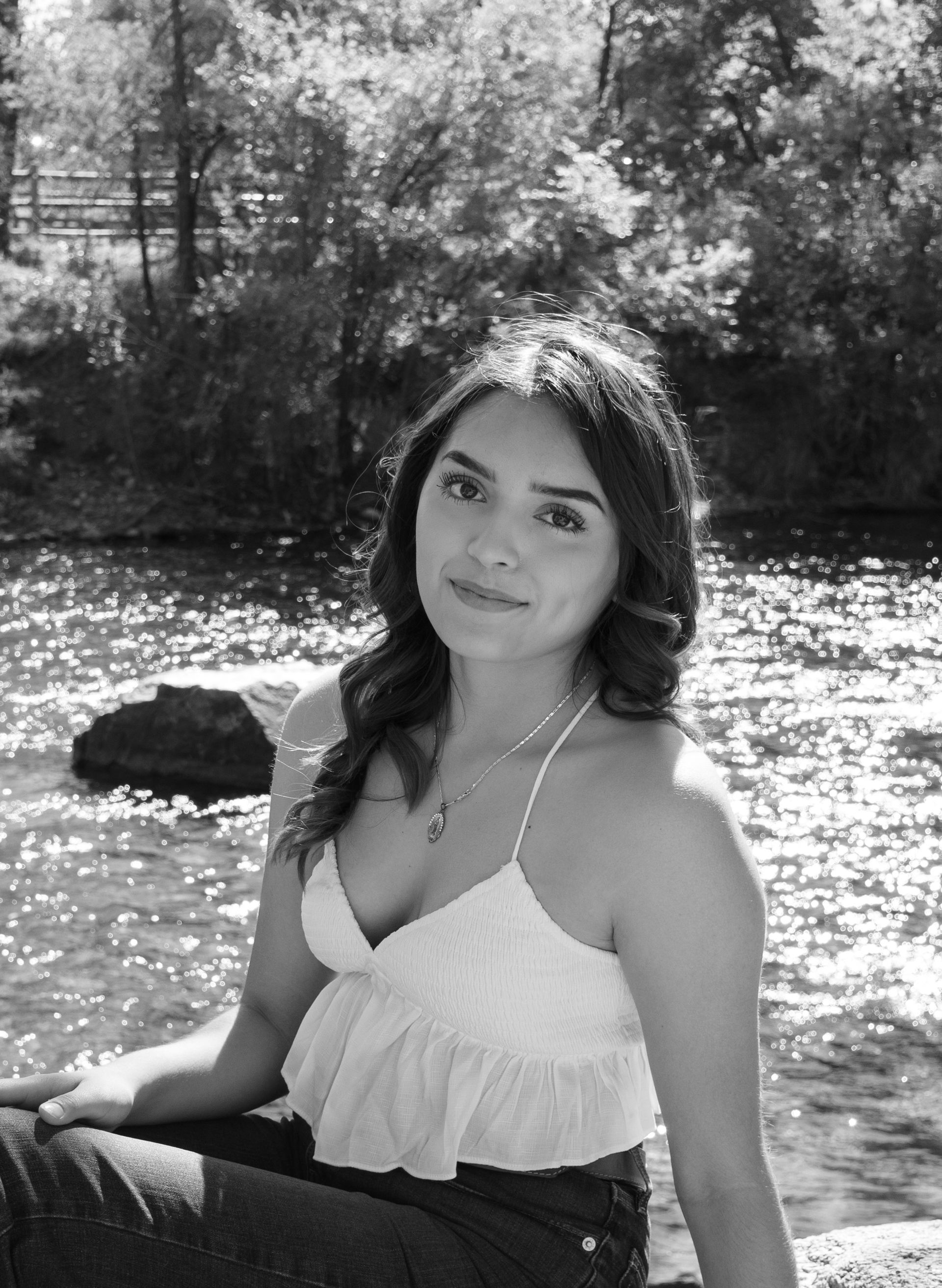 A woman is sitting on a rock near a river in a black and white photo.