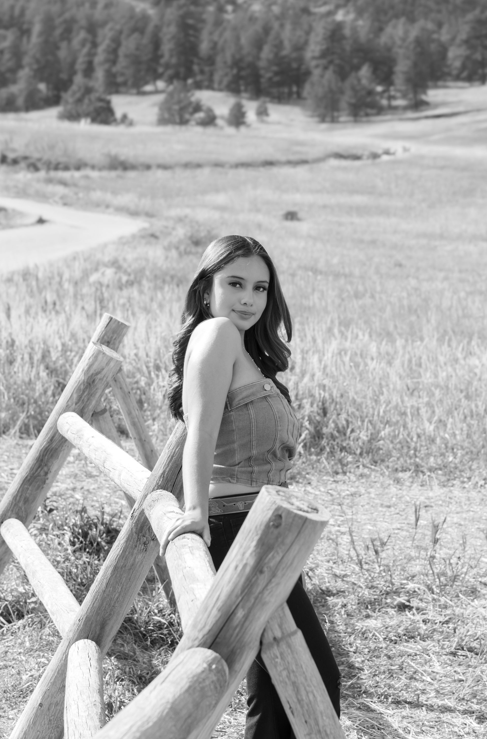 A woman is standing next to a wooden fence in a field.