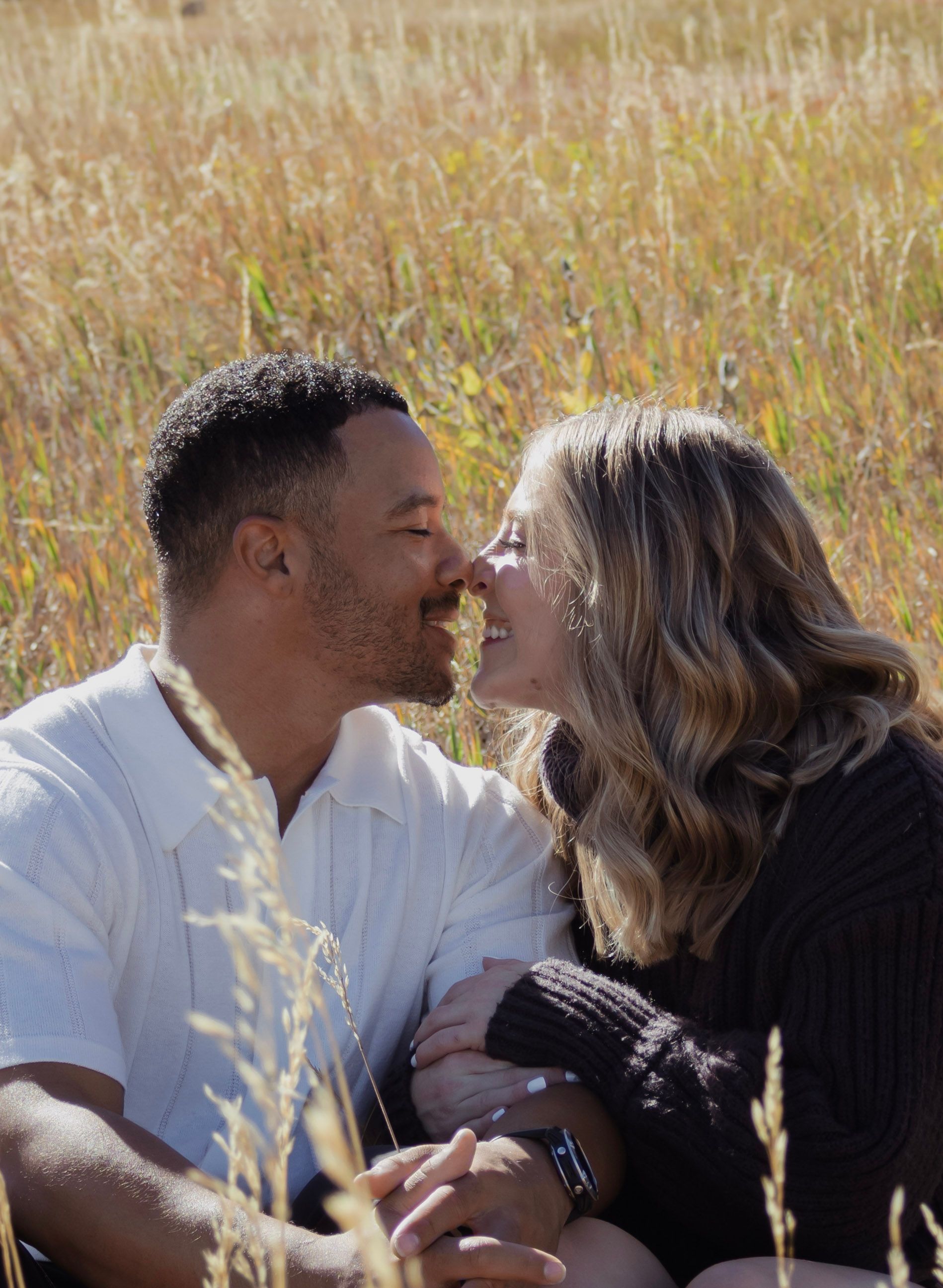 A man and a woman are kissing in a field of tall grass.