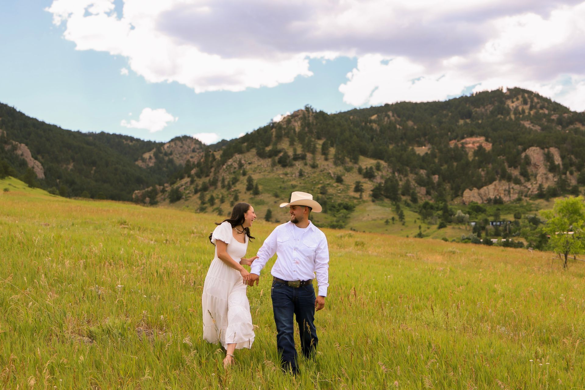 A man and a woman are walking through a grassy field holding hands.