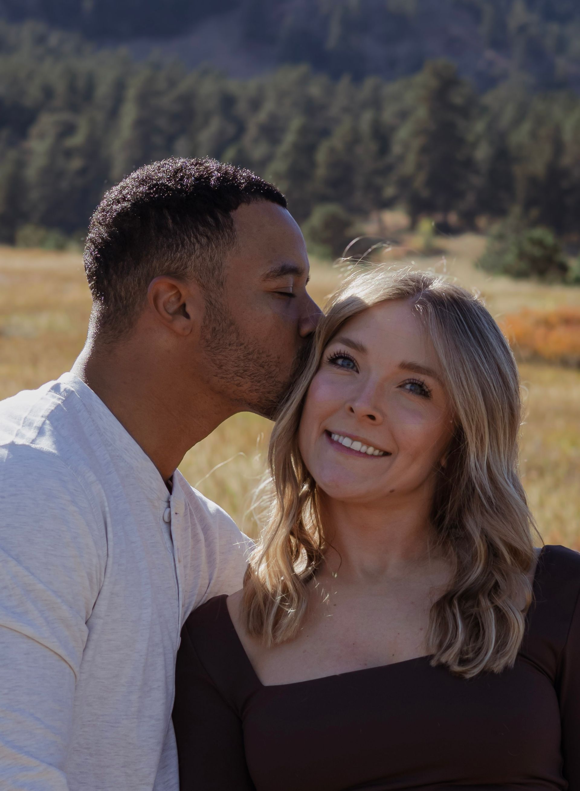 A man is kissing a woman on the cheek in a field.