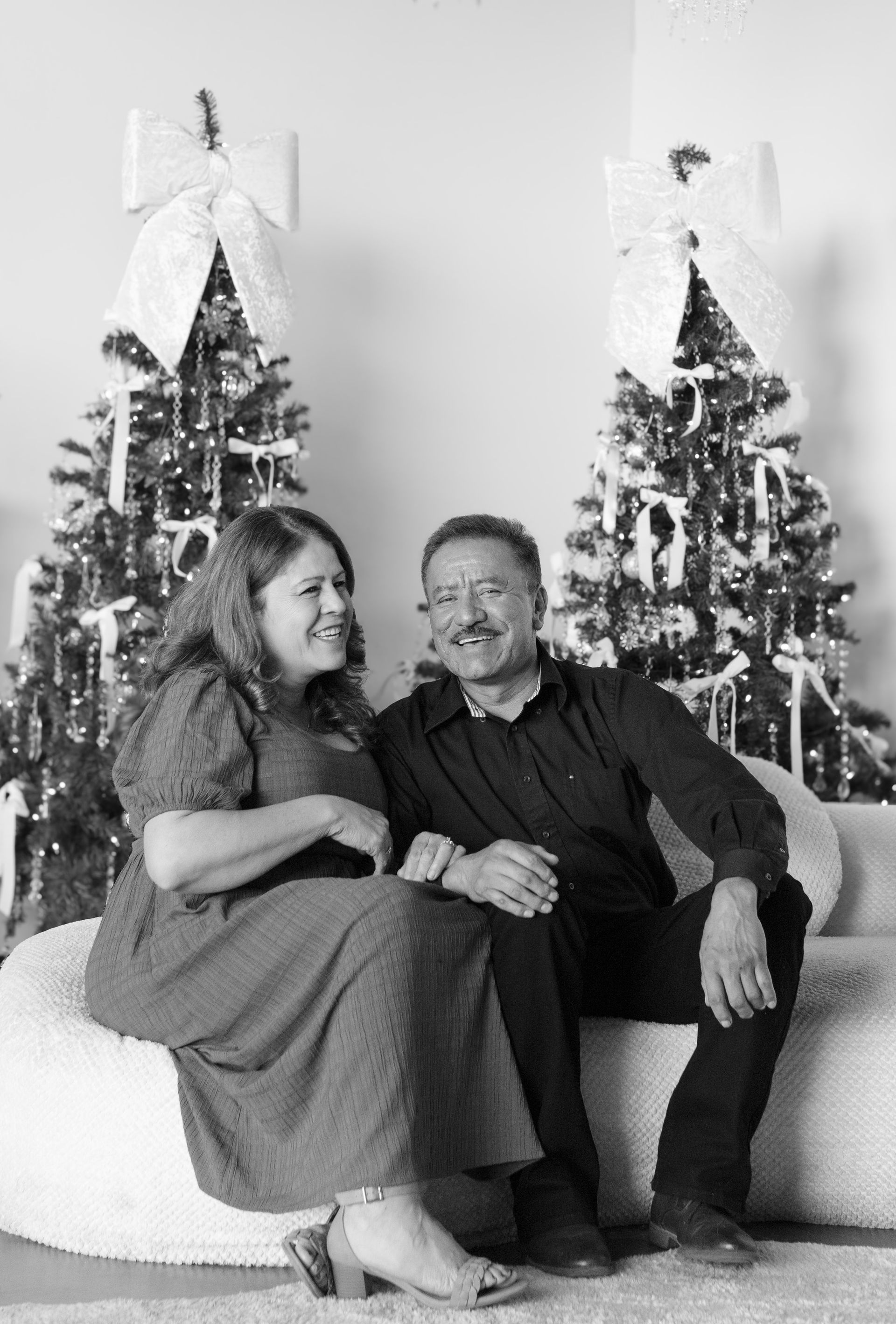 A man and a woman are sitting on a couch in front of a christmas tree.