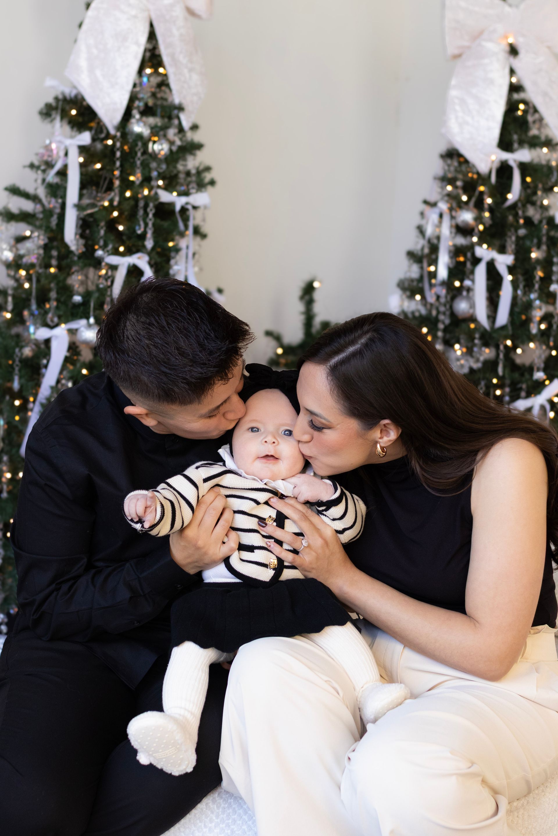 A man and woman are holding a baby in front of a christmas tree.