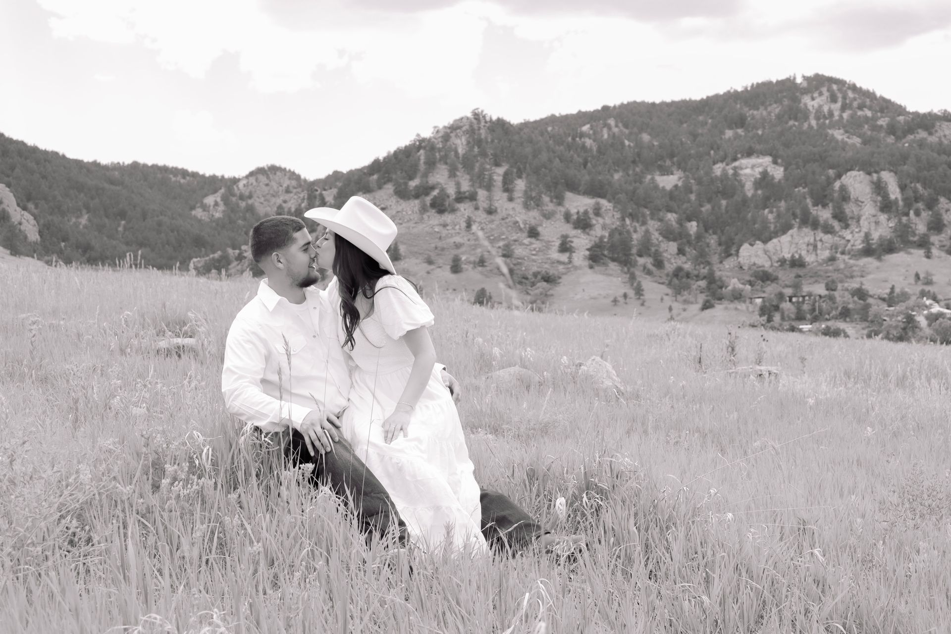A man and a woman are sitting in a field with mountains in the background.
