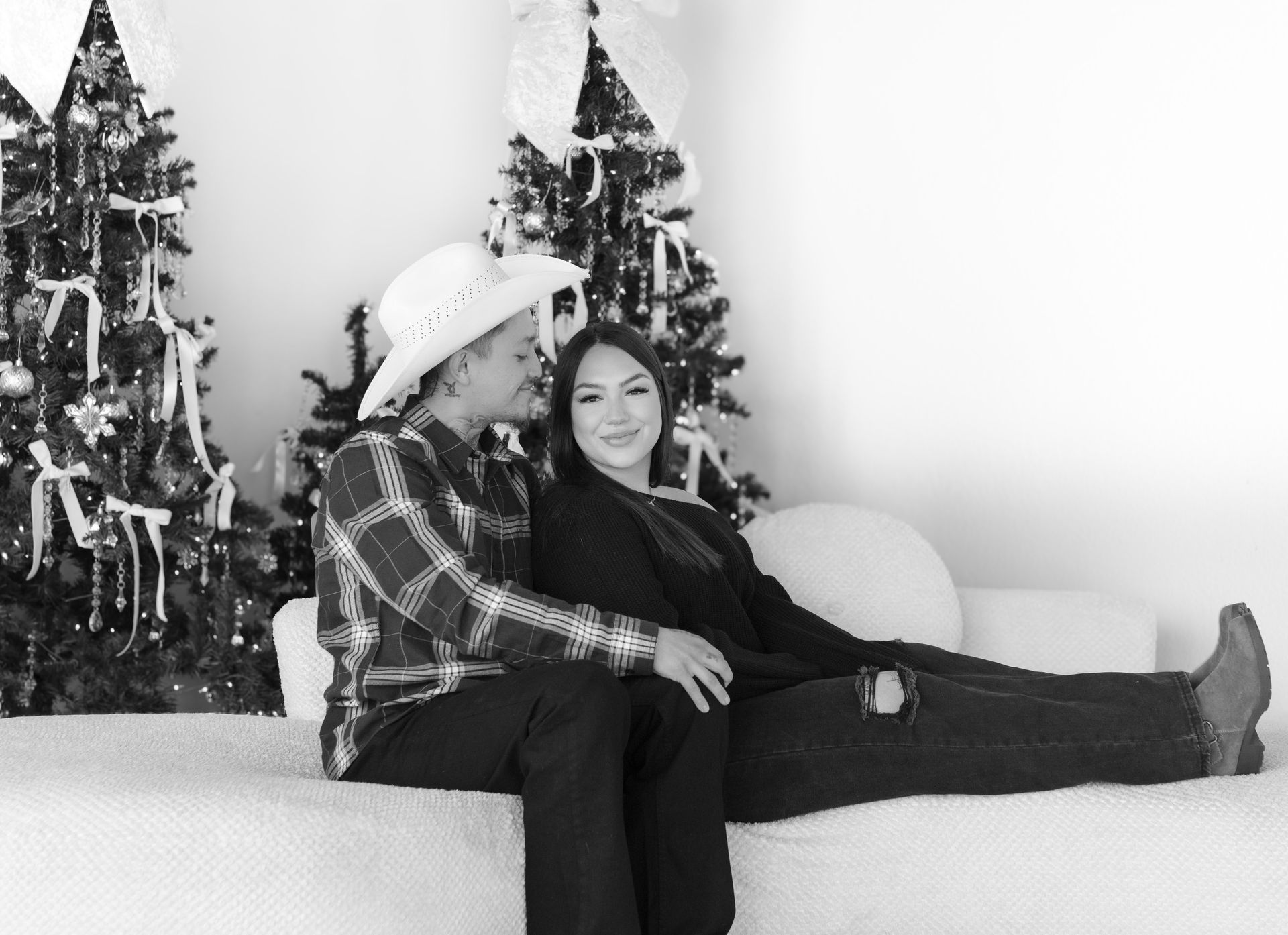A man and a woman are sitting on a couch in front of a christmas tree.