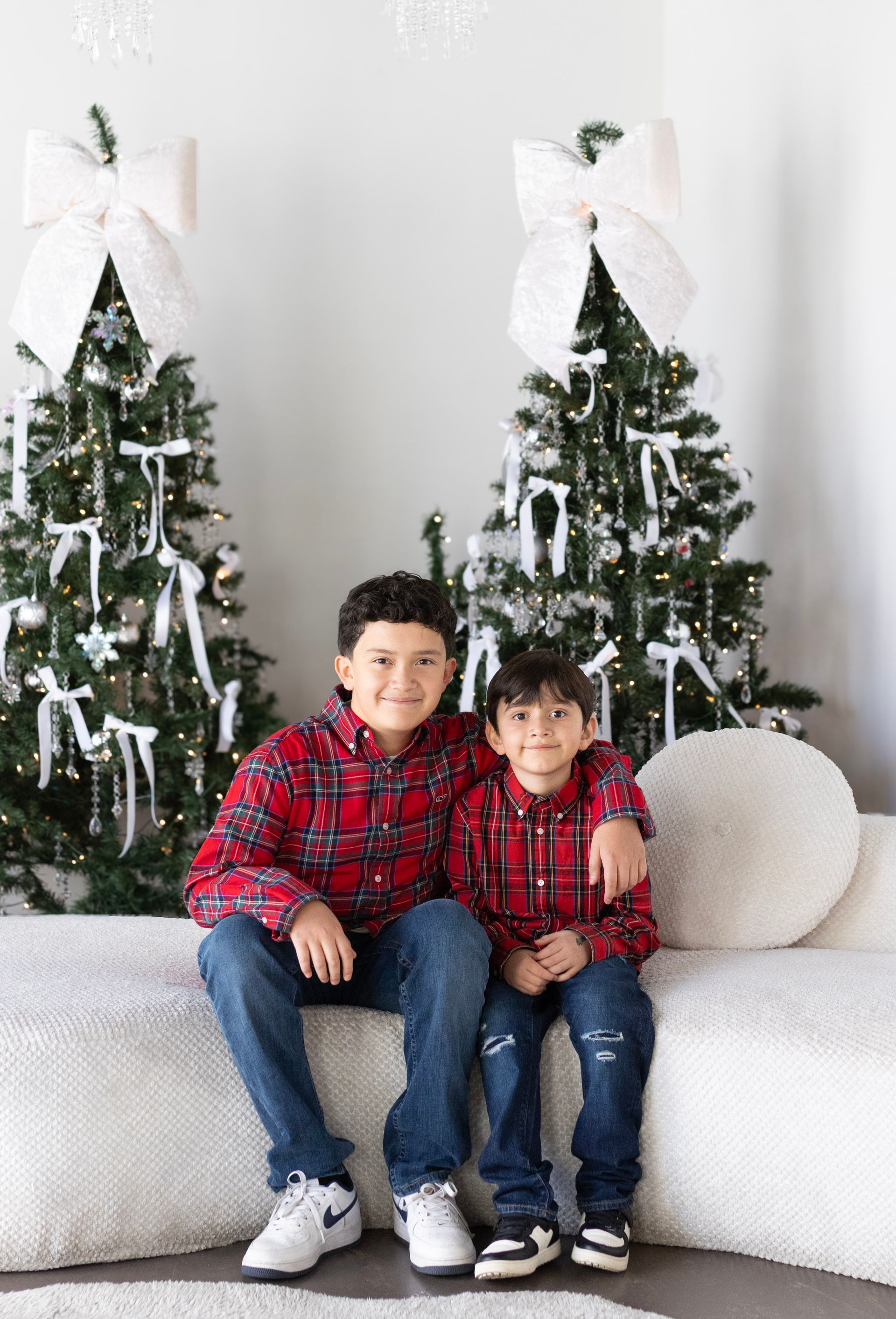 Two boys are sitting on a couch in front of a christmas tree.