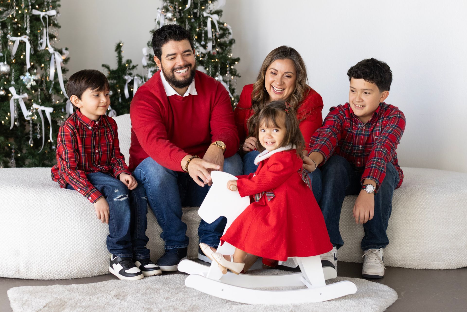 A family is posing for a picture with a rocking horse in front of a christmas tree.