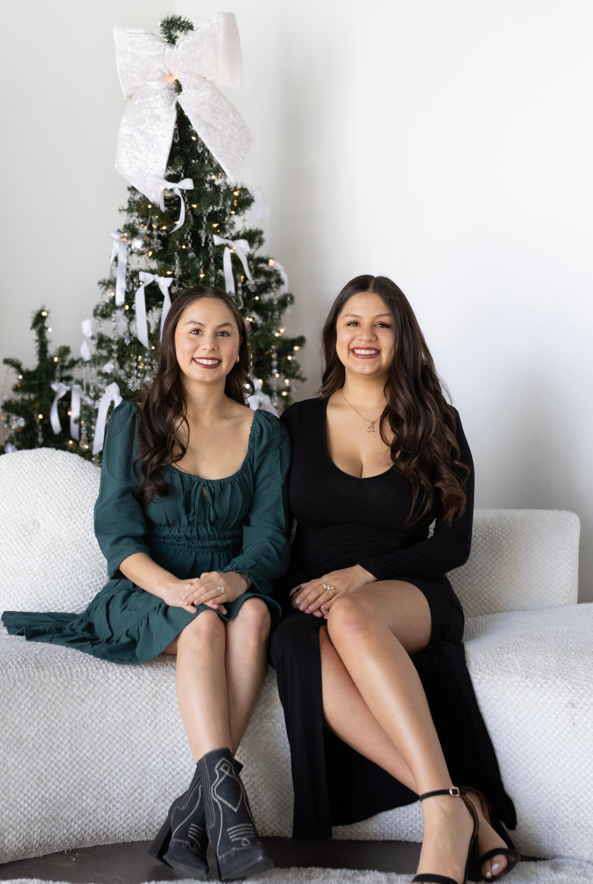 Two women are sitting on a couch in front of a christmas tree.