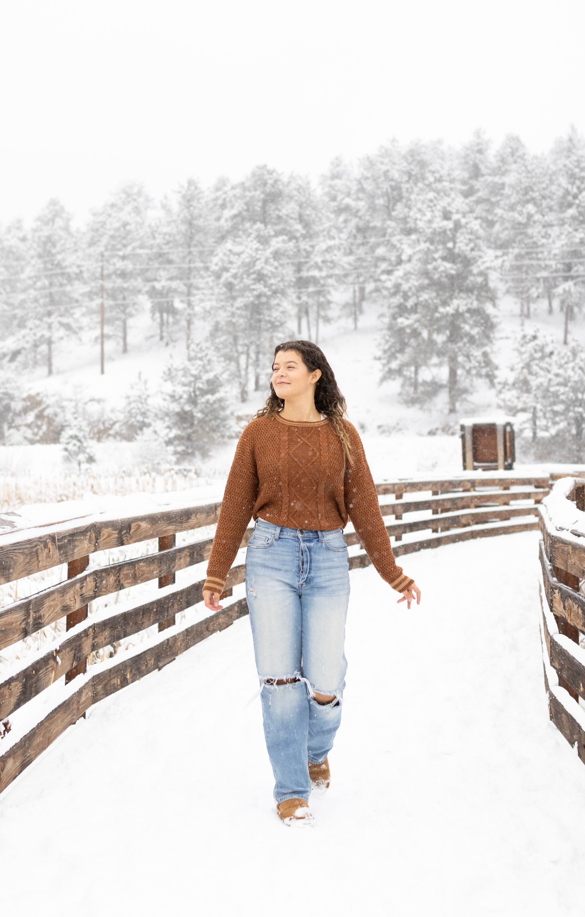 A woman is walking in the snow on a wooden bridge.