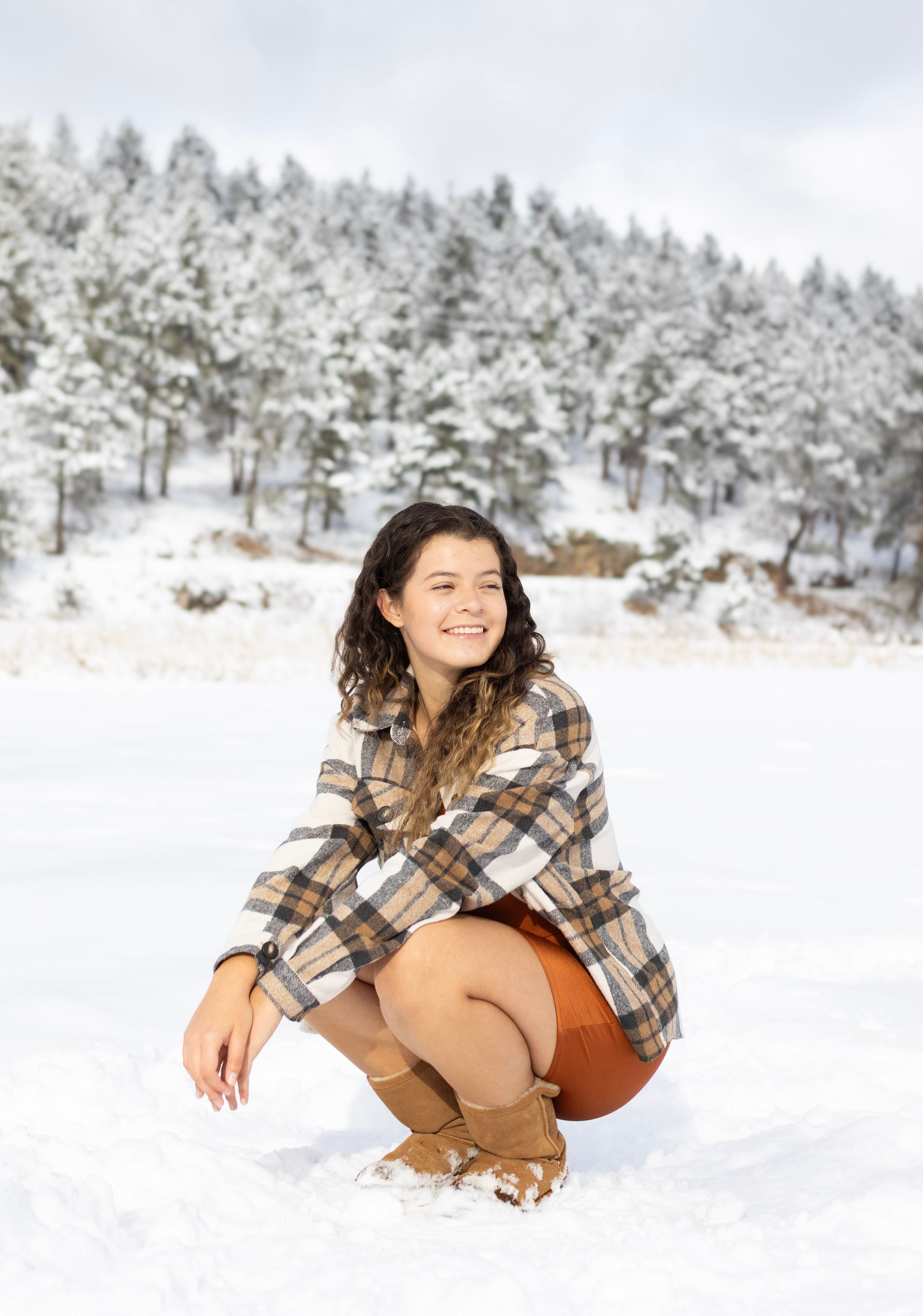 A woman in a plaid shirt is squatting in the snow.