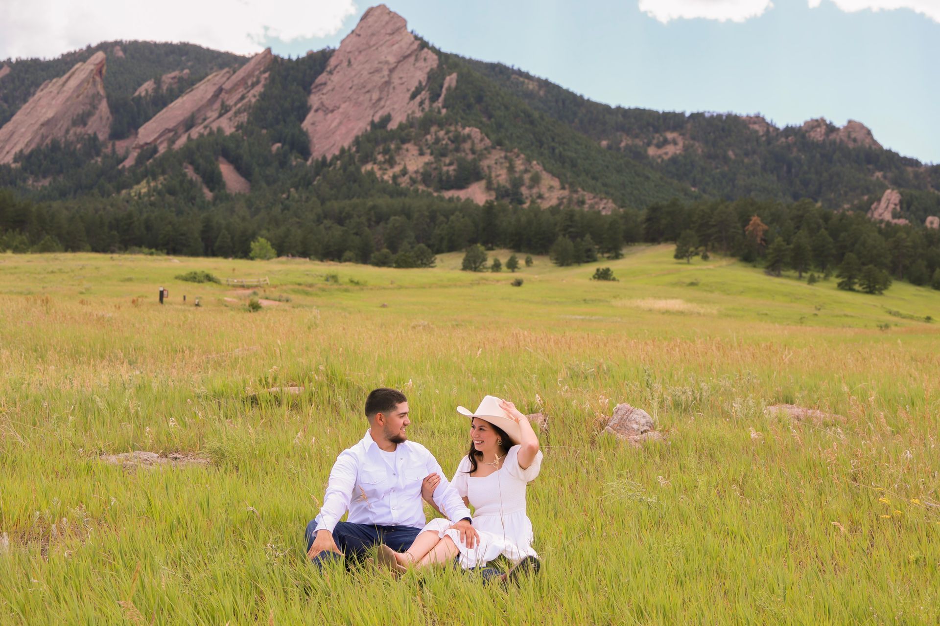 A man and a woman are sitting in a field with mountains in the background.