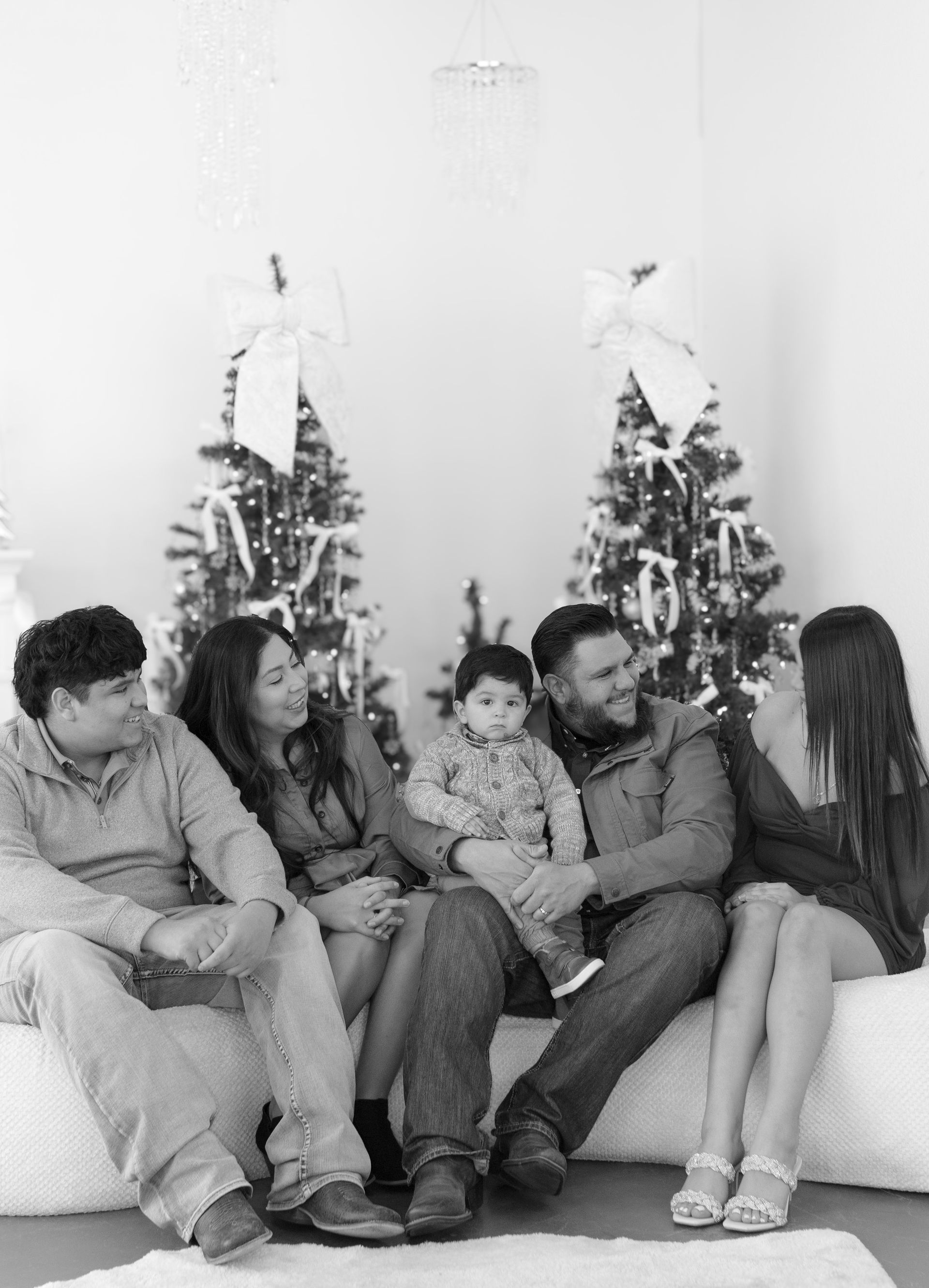 A black and white photo of a family sitting on a couch in front of a christmas tree.