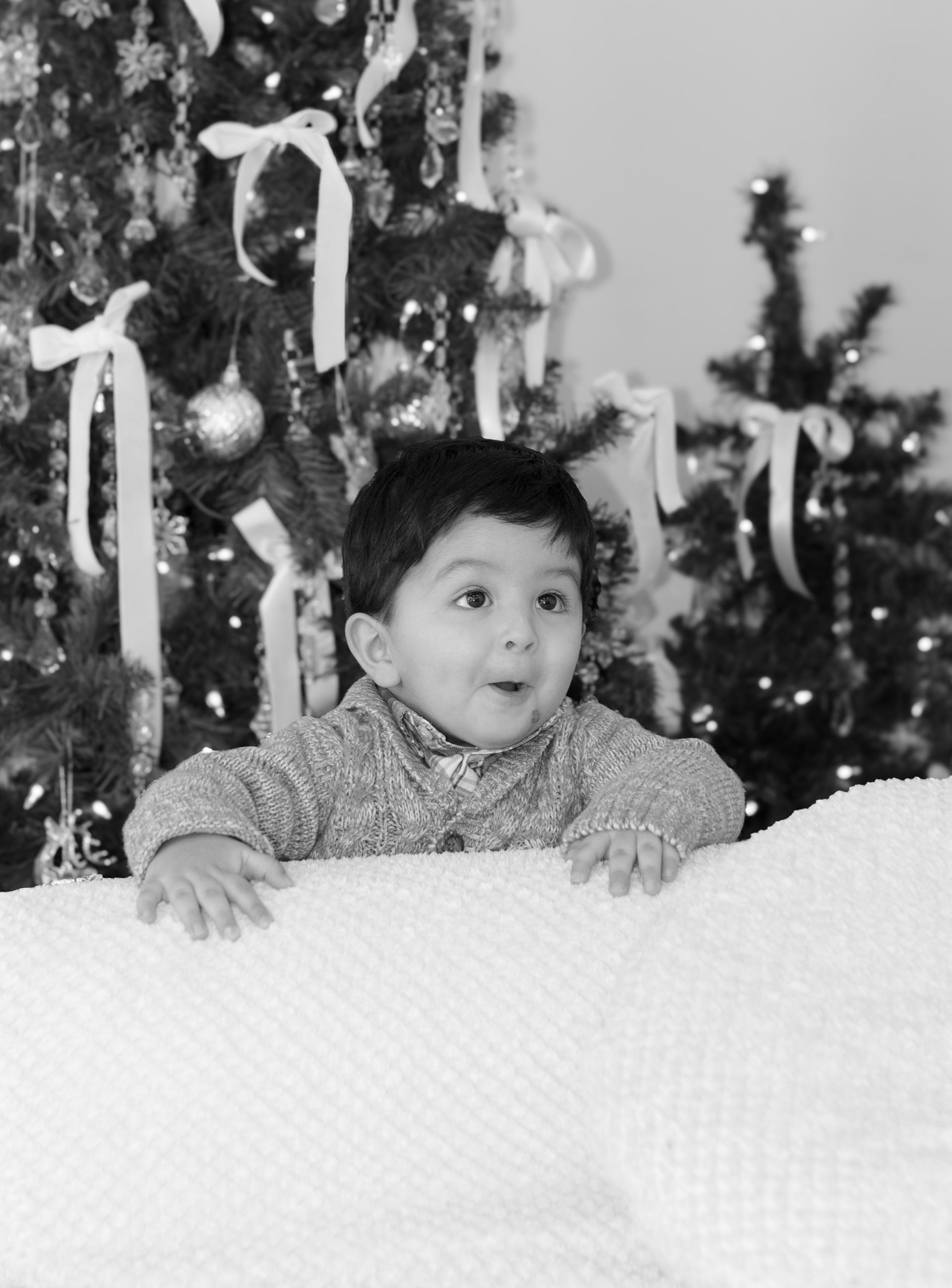 A black and white photo of a little boy in front of a christmas tree