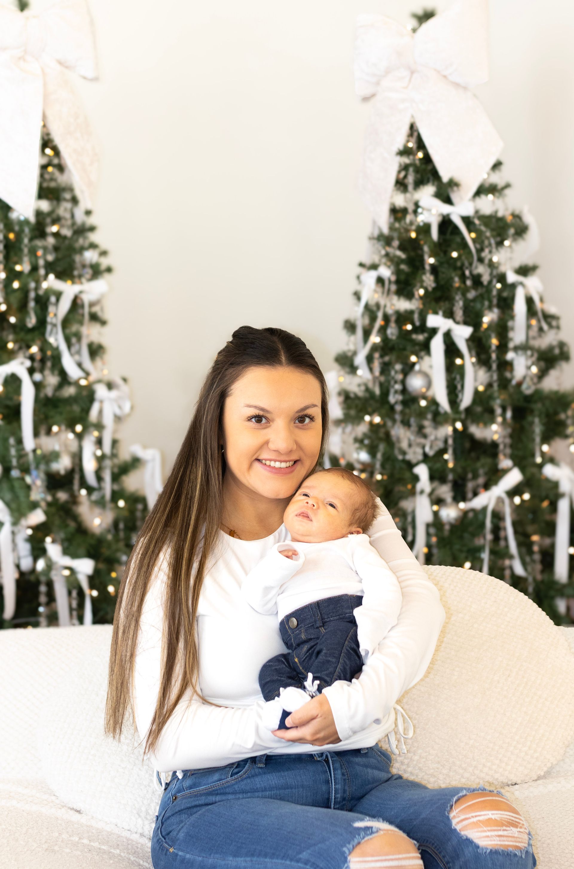 A woman is sitting on a couch holding a baby in front of a christmas tree.