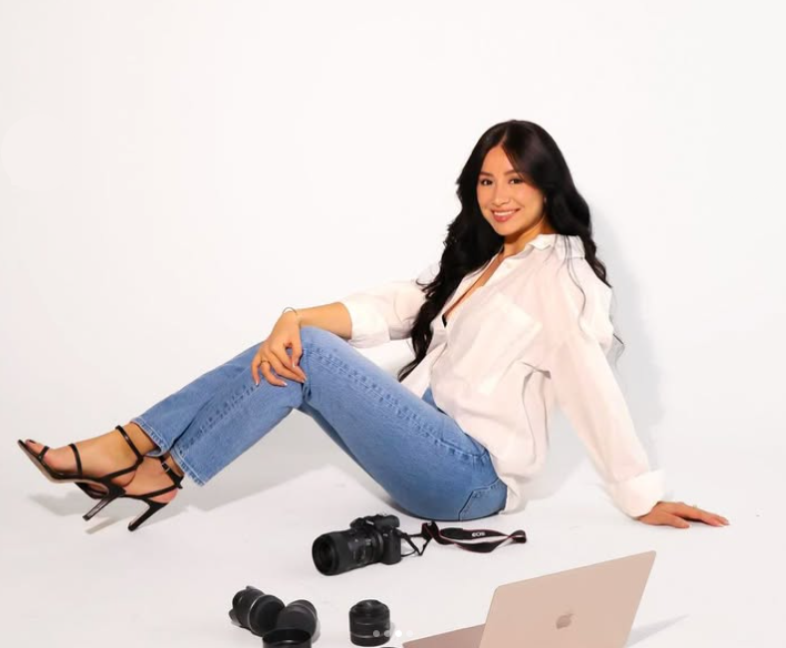 A woman is sitting on the floor next to a laptop and cameras