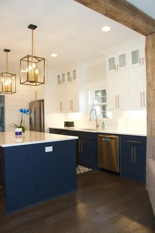 Modern kitchen with blue and white cabinets, gold hardware, and a dark wooden floor.