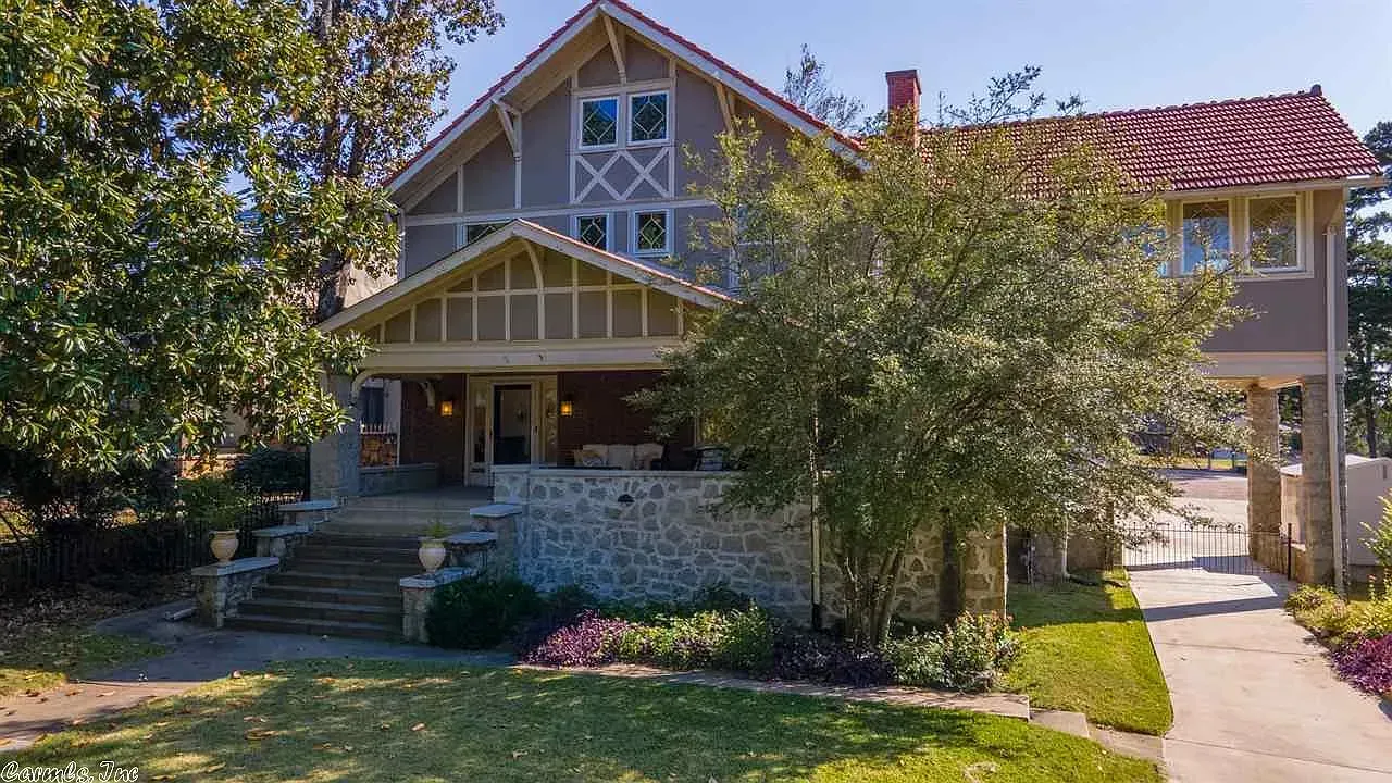 Two-story house with stone facade, porch, red roof, and a driveway lined with purple flowers.