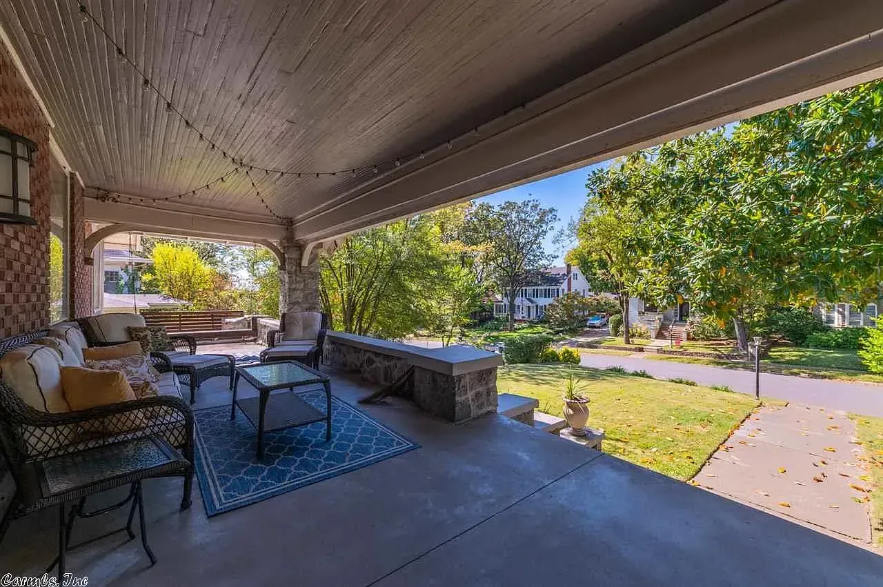 Covered porch with seating; a small table on a blue rug faces the street with trees and other houses.