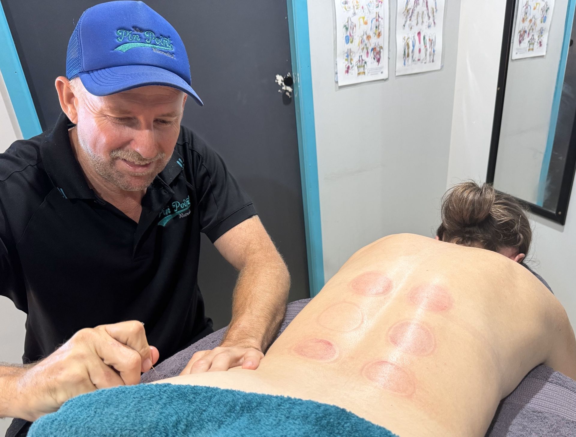 A Man In A Blue Scrub Is Standing Next To A Blue Table — Pin Point Remedial Massage In Lammermoor, QLD