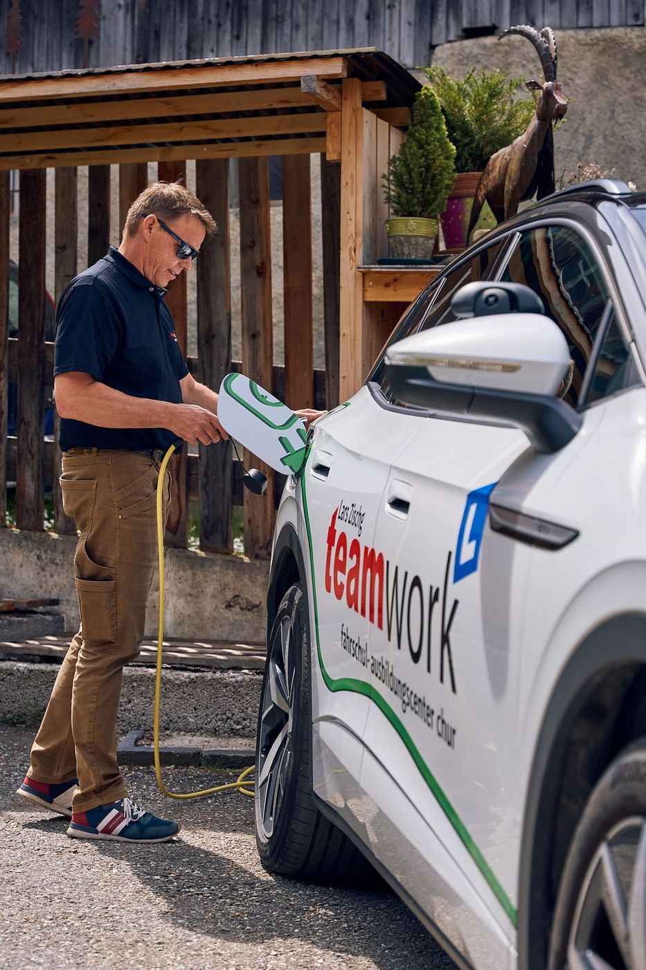 Fahrlehrer Lars Zischg lädt ein Elektroauto auf, auf dessen Seite Teamwork steht