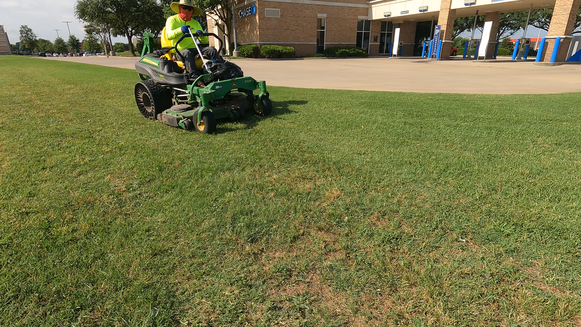 Person on a John Deere lawnmower mowing grass near a building on a sunny day.