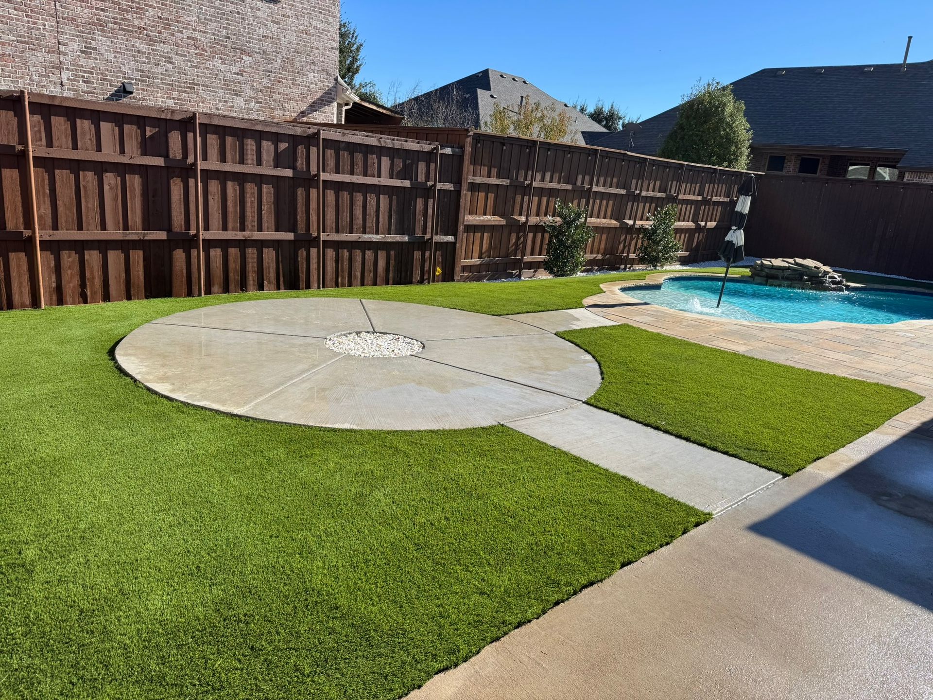 Backyard with artificial grass, a circular patio, pool, and wooden fence.