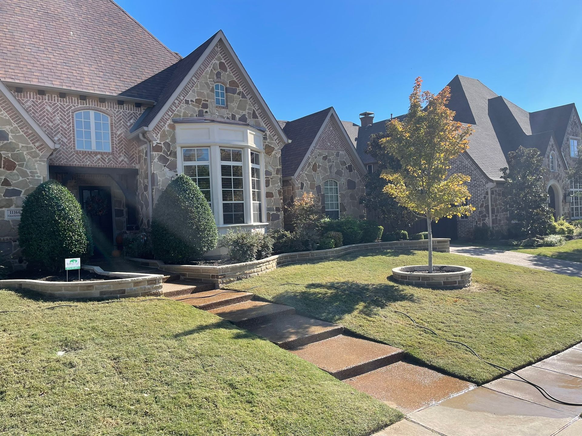 A multi-gabled stone and brick house with manicured lawn under a clear blue sky.