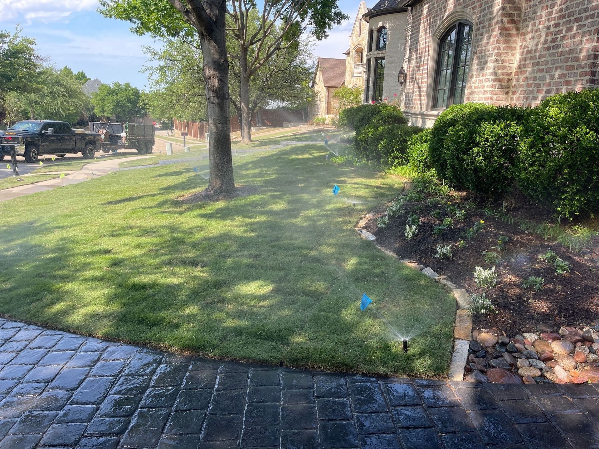 Sprinklers watering a green lawn next to a brick home.