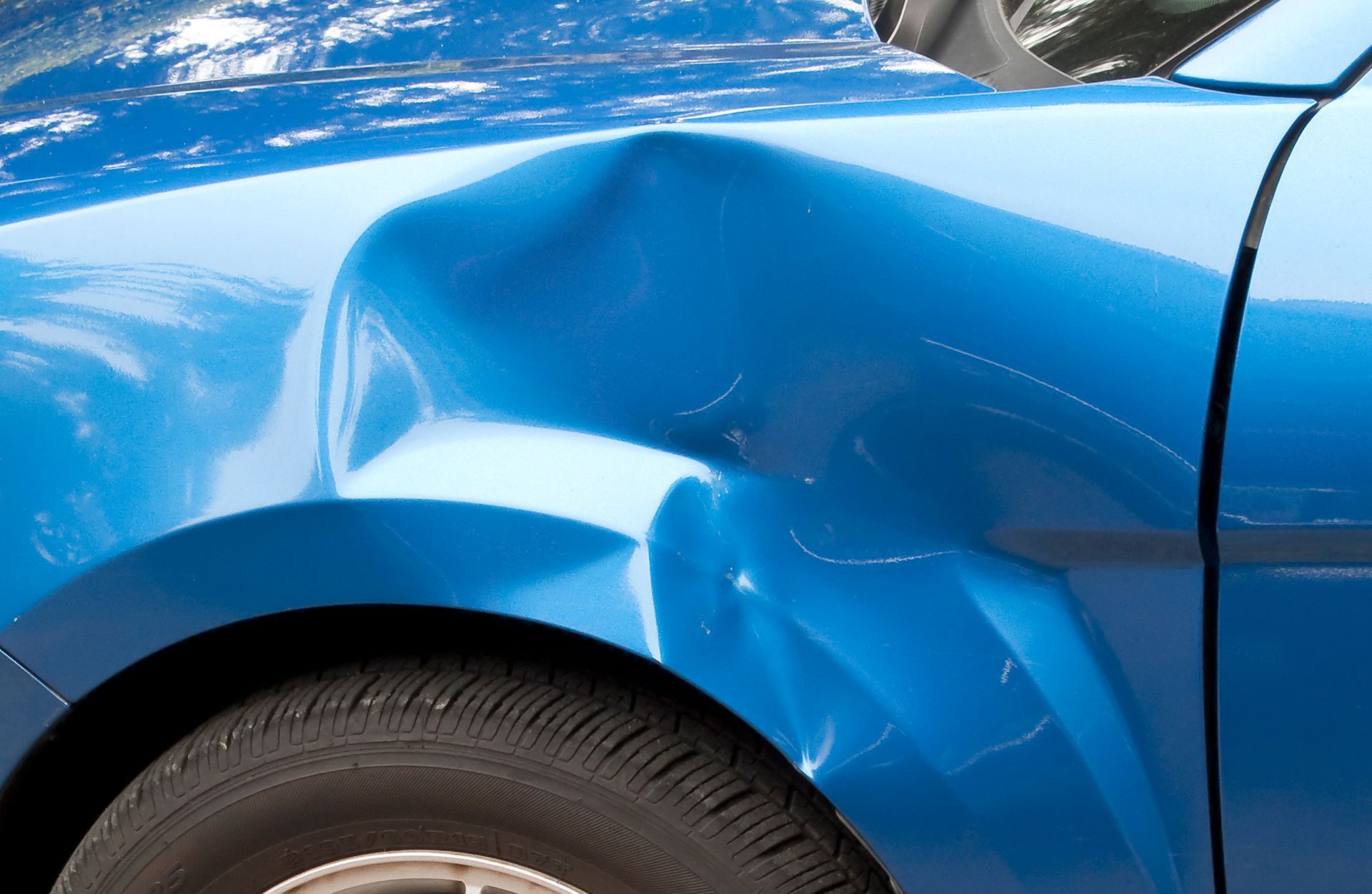 Close-up of a blue car with a dented fender.