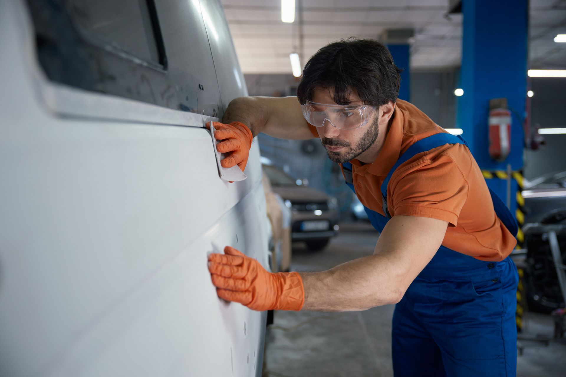 An auto body shop technician repairing and smoothing a vehicle exterior panel.