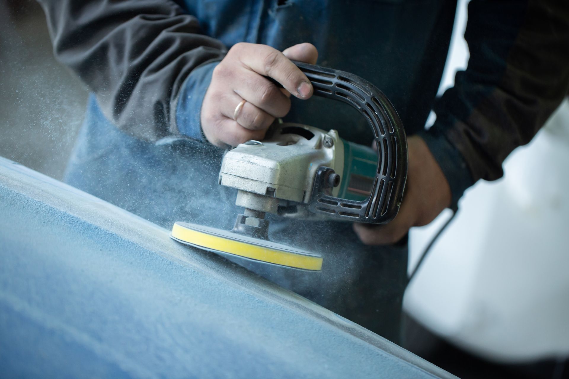 Auto body shop technician sanding vehicle surface during repair preparation.
