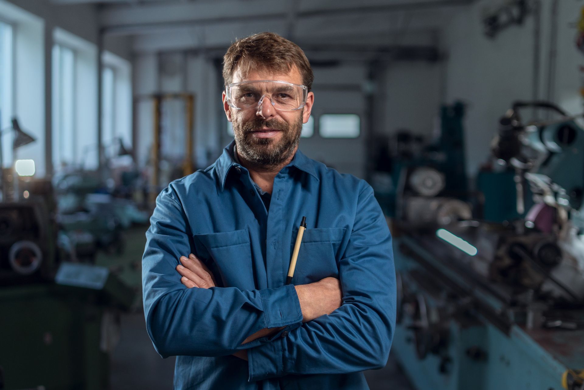 Mechanic in blue uniform standing in auto shop with arms crossed. Mechanic in blue uniform standing in auto shop with arms crossed.
