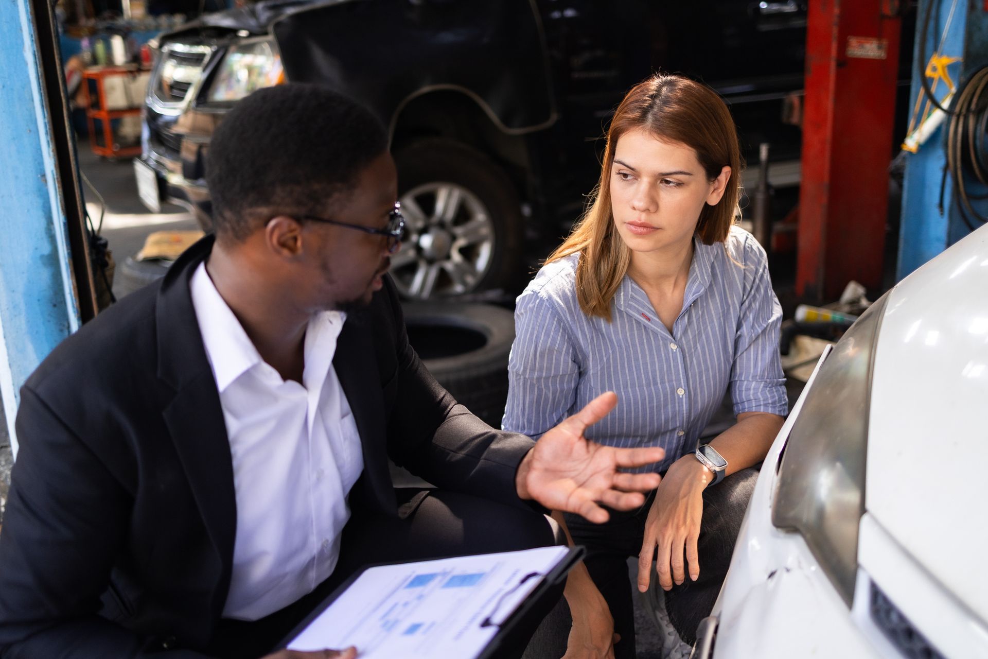Two people discussing car maintenance in an auto repair shop. Two people discussing car maintenance in an auto repair shop.