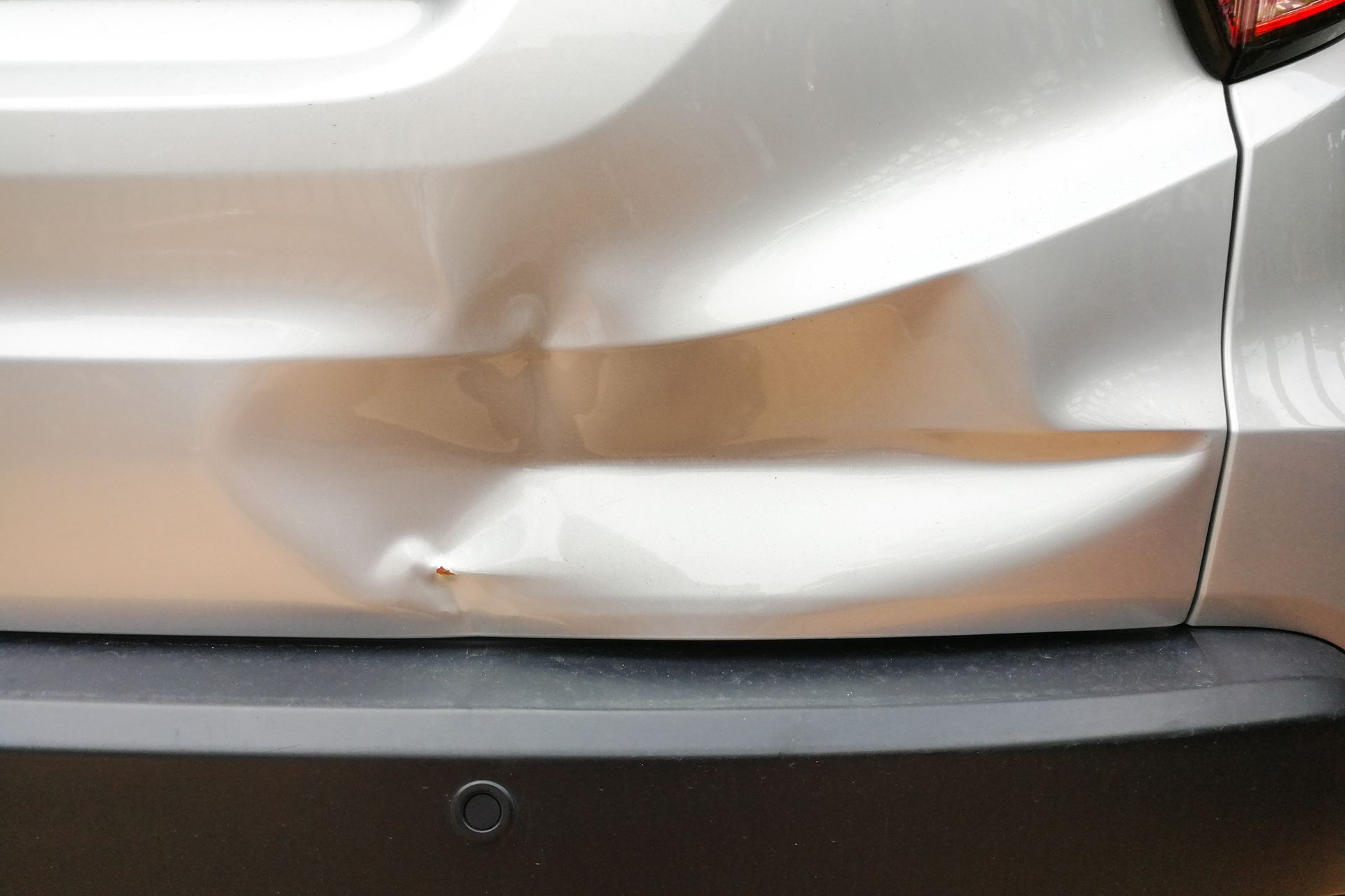 Closeup of small dent of silver car’s rear, representing auto collision repair services. Closeup of small dent of silver car’s rear, representing auto collision repair services.