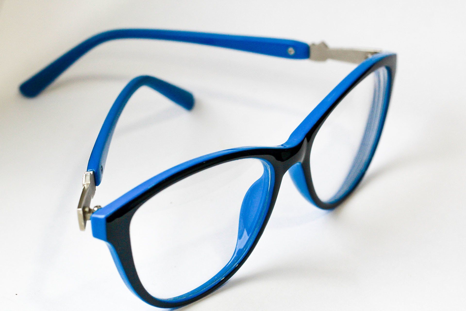 Blue and black eyeglasses on a white surface, with one lens in focus.