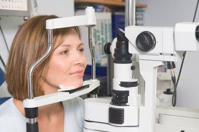 Woman at an eye exam looking through a slit lamp in a doctor's office.