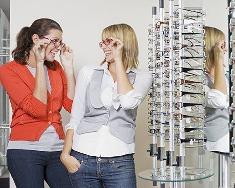 Two women in eyeglasses store looking at and trying on eyewear.
