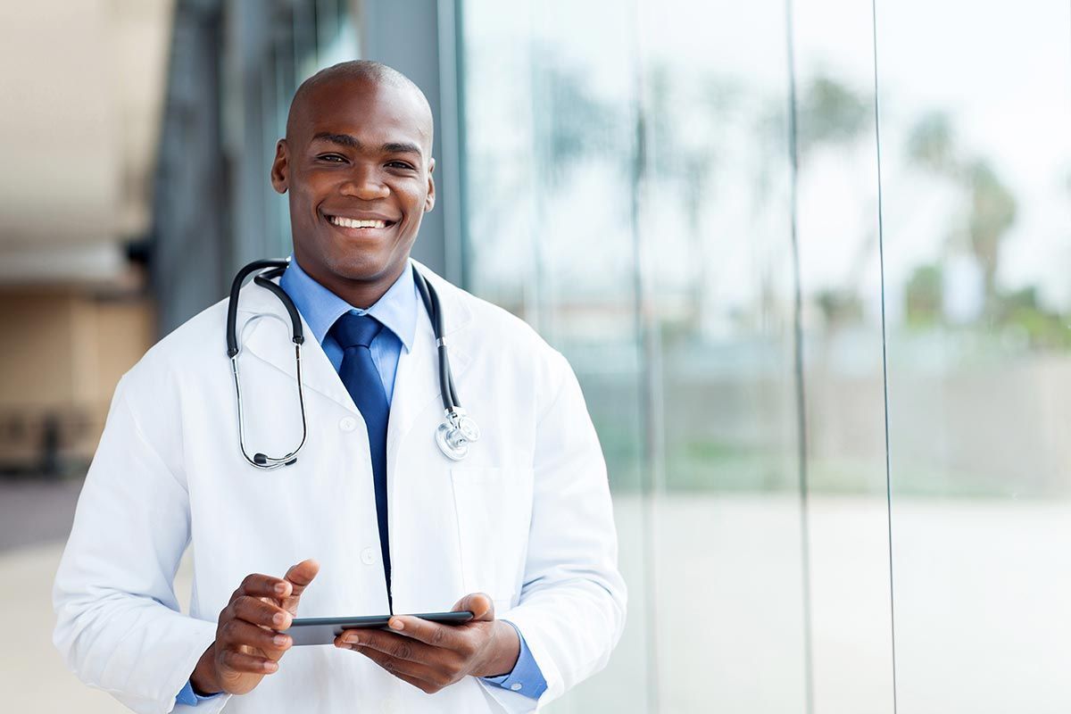 Doctor with stethoscope holding tablet, smiling in a modern hallway.