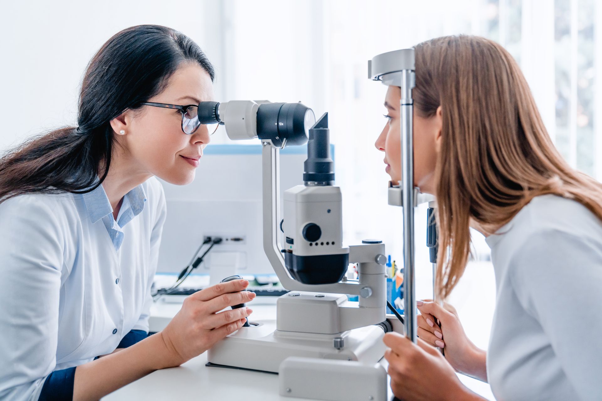Eye care professional examining a patient with a slit lamp during an eye exam.]