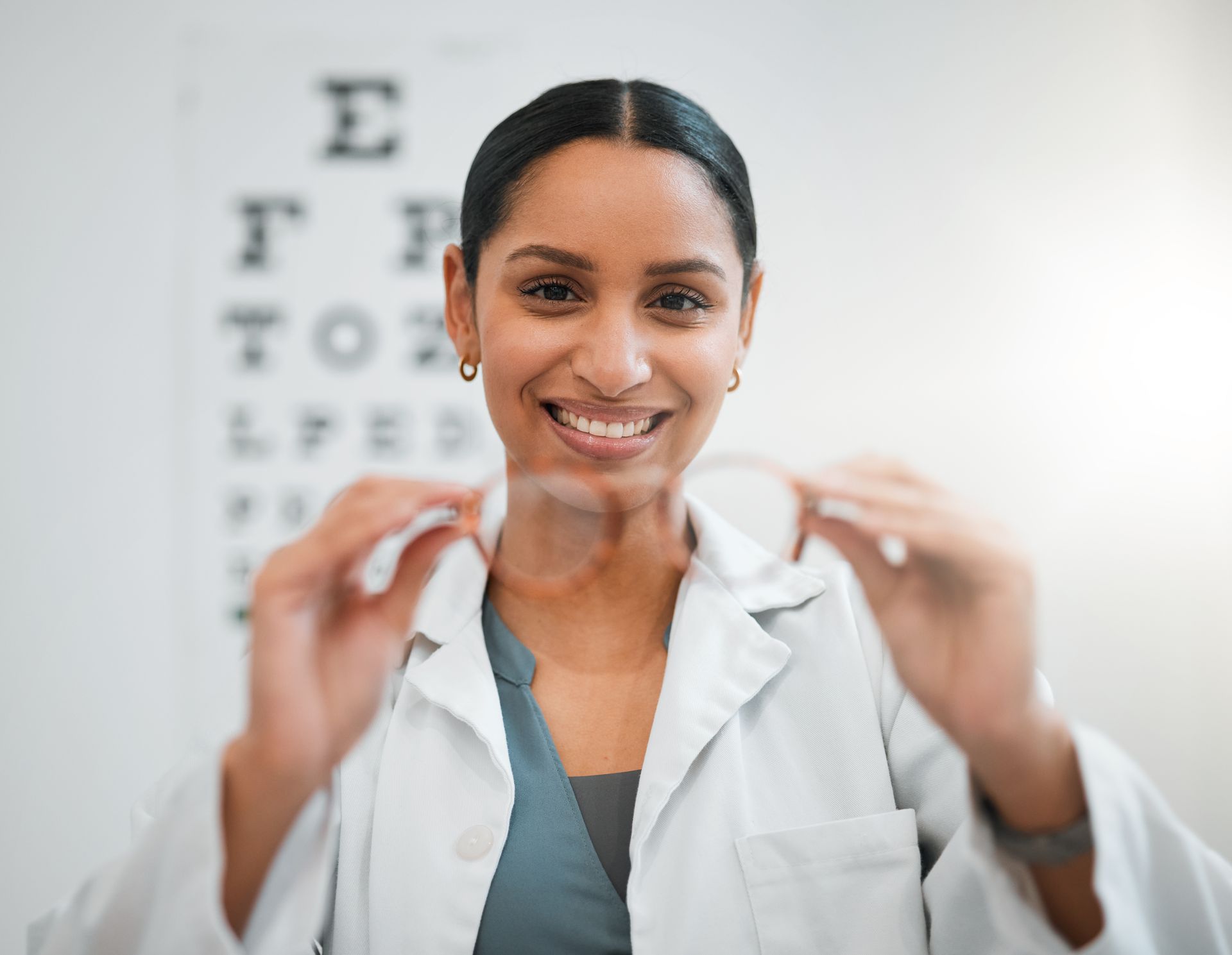 Optometrist adjusting eyeglasses in a clinic with an eye chart in the background. 