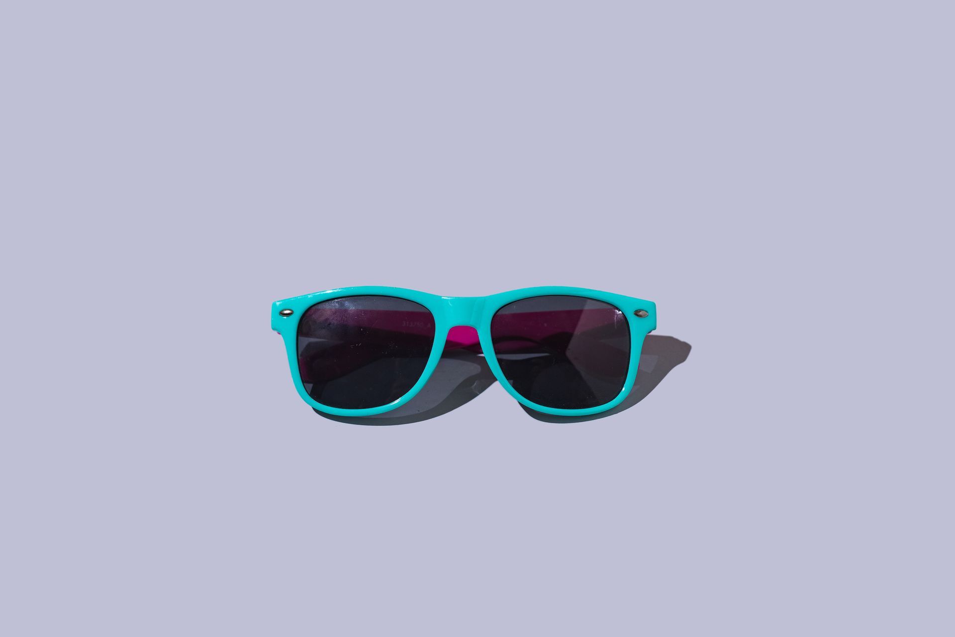 Teal sunglasses with pink accents on a light purple background. Teal sunglasses with pink accents on a light purple background.