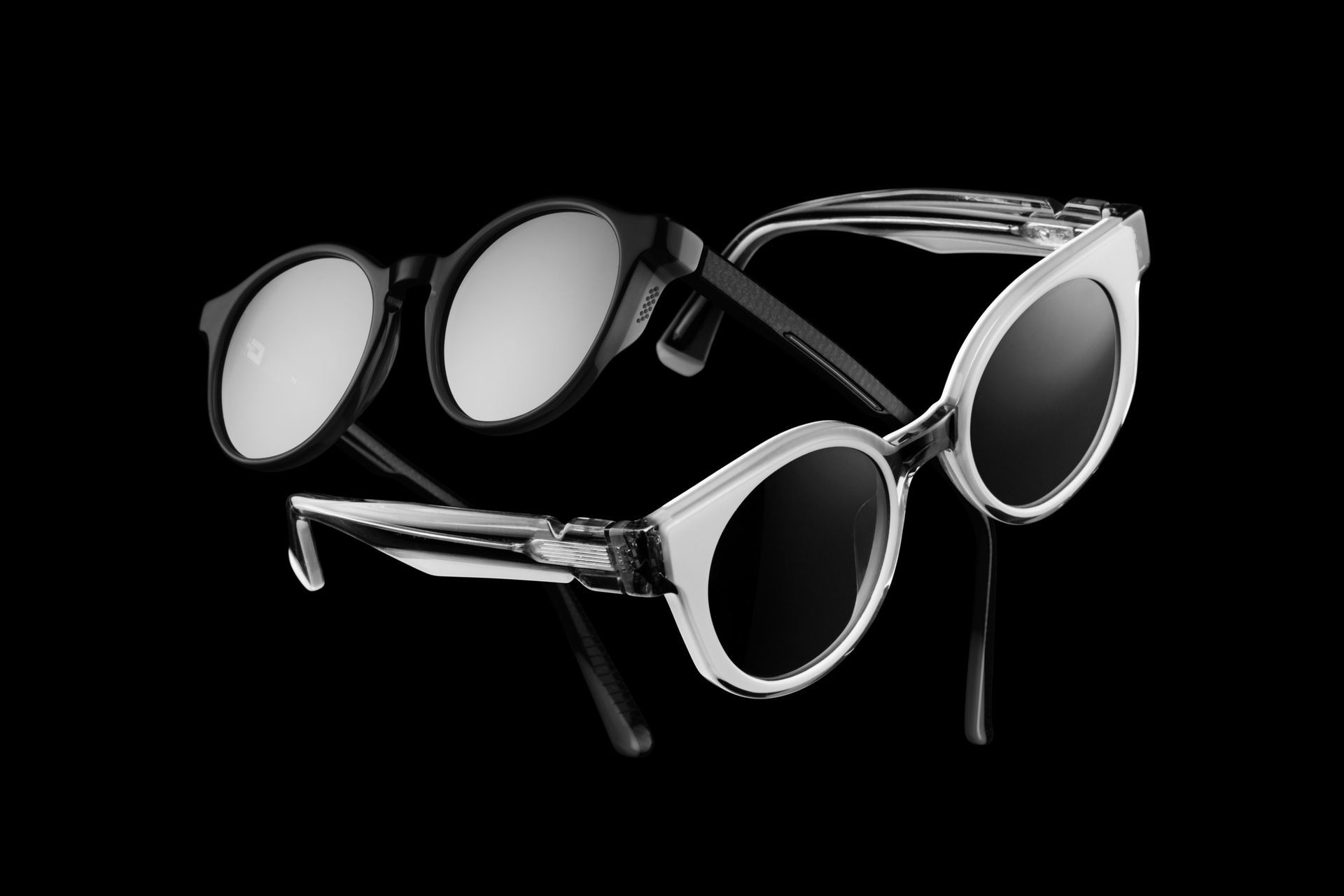 Two pairs of sunglasses, one black, one white, set against a black background. Two pairs of sunglasses, one black, one white, set against a black background.