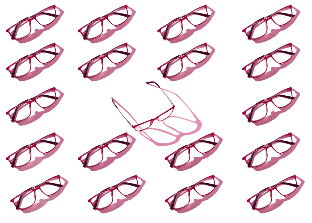 Rows of pink-framed eyeglasses, one pair upright, casting a shadow on a white background.