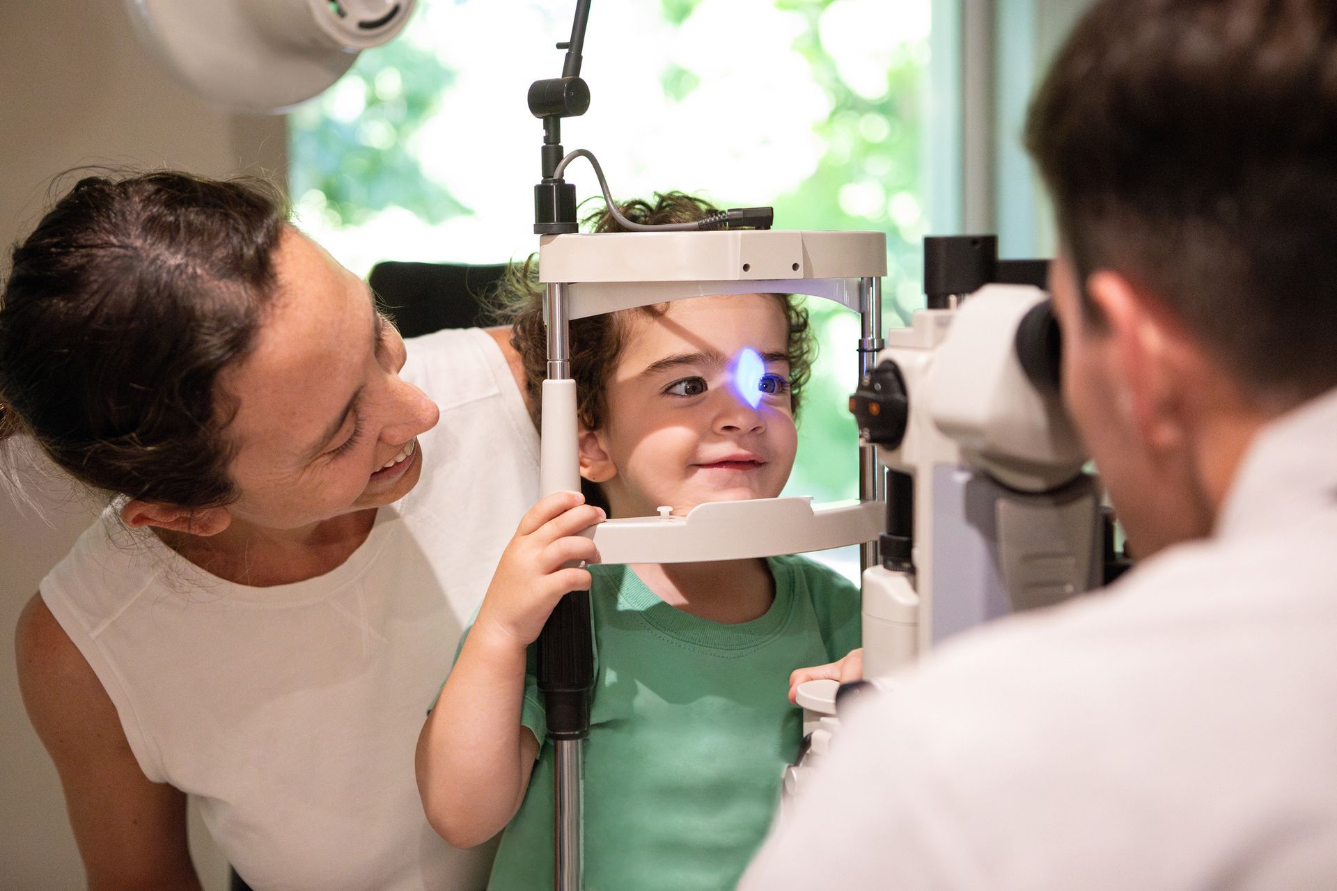Woman comforts child during eye exam by doctor.