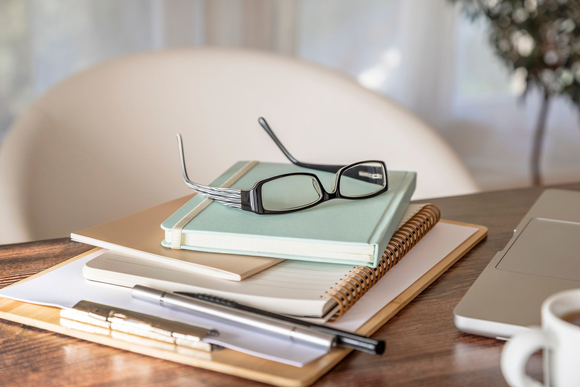 Desk with notebook, glasses, pen, and laptop; light-blue book on top. Desk with notebook, glasses, pen, and laptop; light-blue book on top.